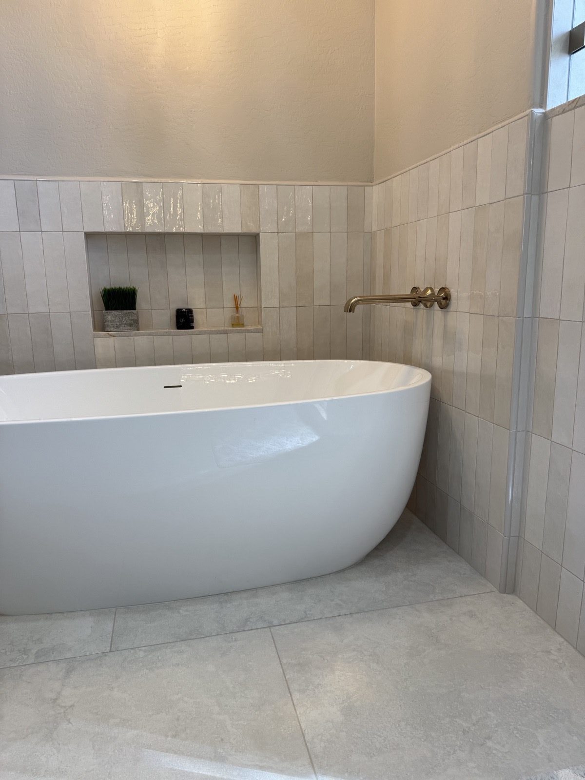 Luxury freestanding soaker tub with vertical stacked tile feature wall, brushed gold fixtures, and large format stone floor -- a finished Level Up Tile bathroom in Peoria AZ