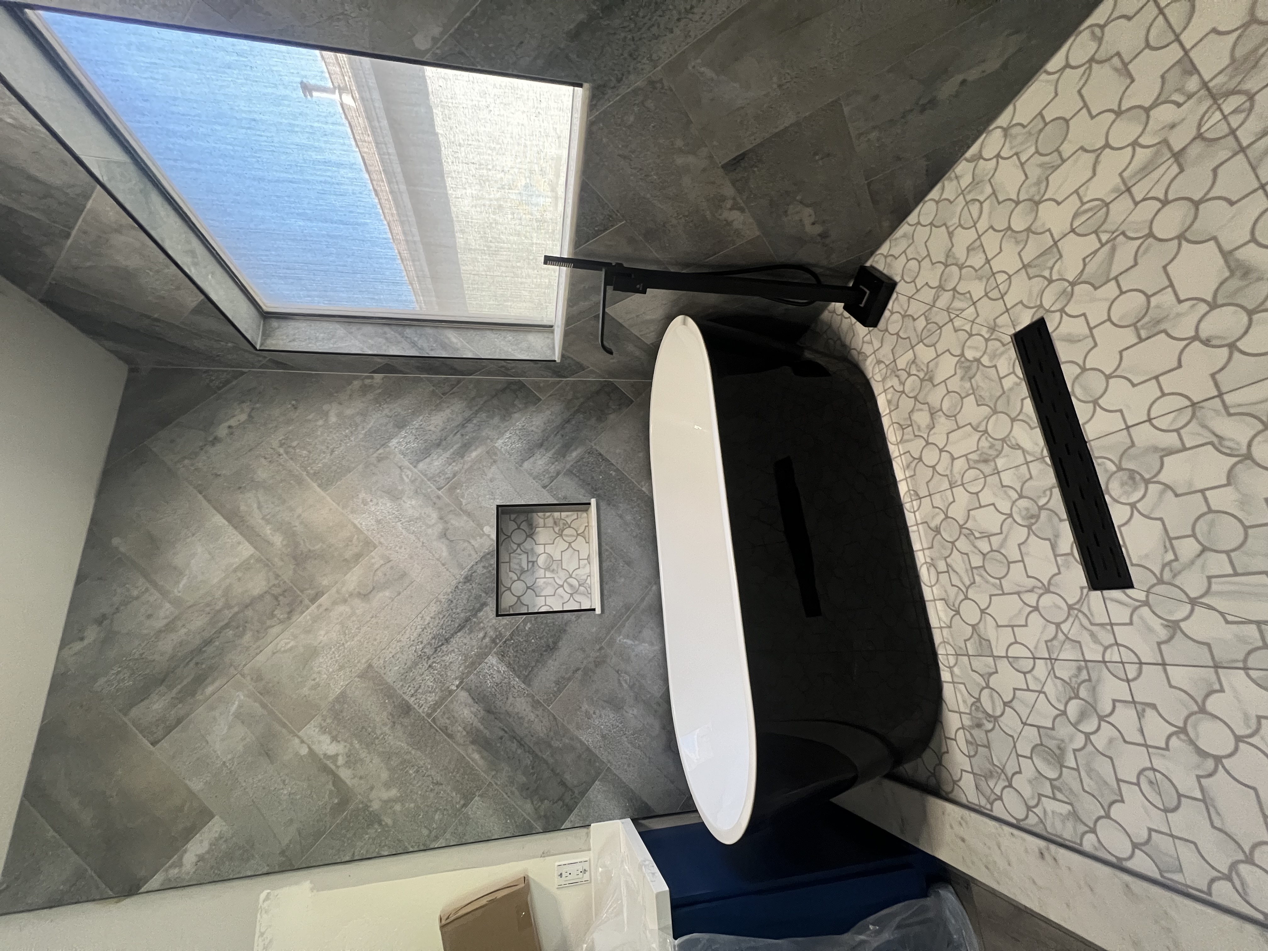 Gray herringbone tub surround with mosaic accent and freestanding tub by Level Up Tile