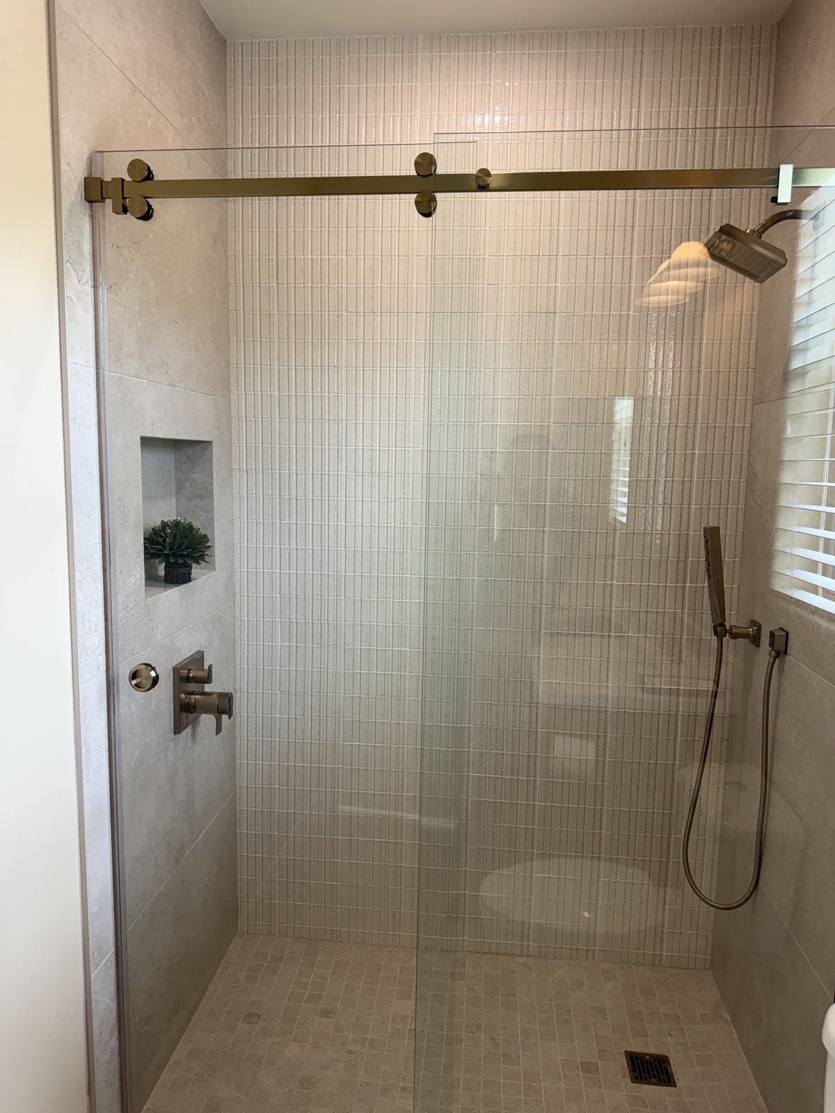 Sliding rail-style glass shower door with brushed gold hardware by Level Up Tile