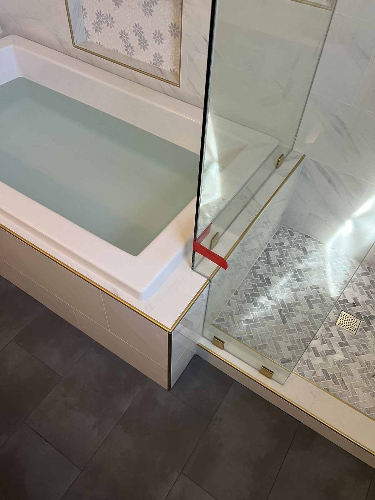 Glass divider panel between tub and shower with brushed gold trim by Level Up Tile
