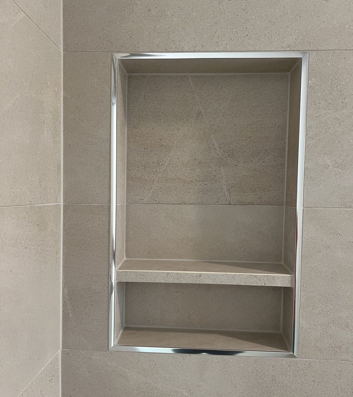 Natural stone shower niche with chrome trim and mitered shelf detail by Level Up Tile in Scottsdale AZ