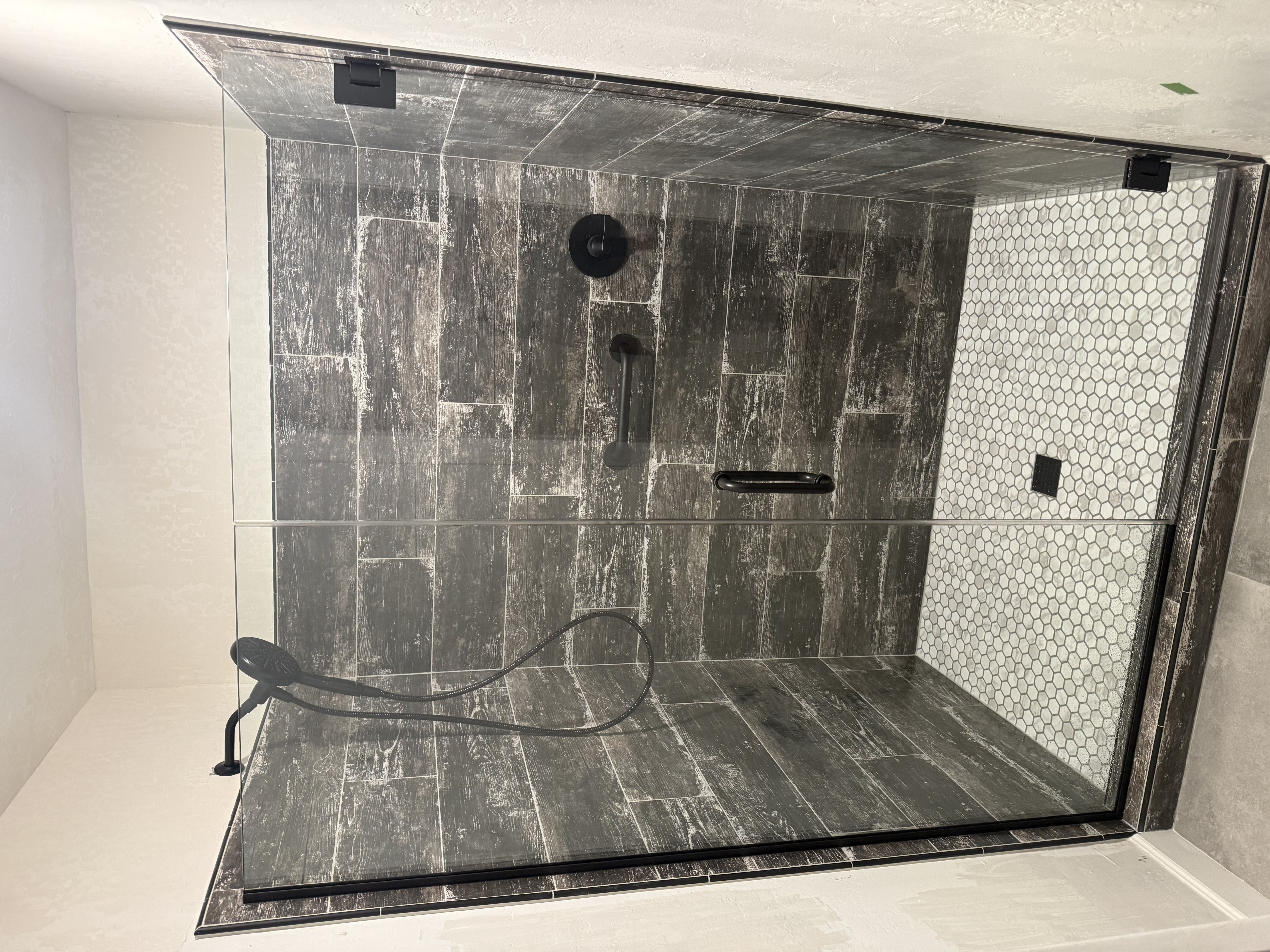 Dark wood-look tile shower with white hexagonal accent wall by Level Up Tile