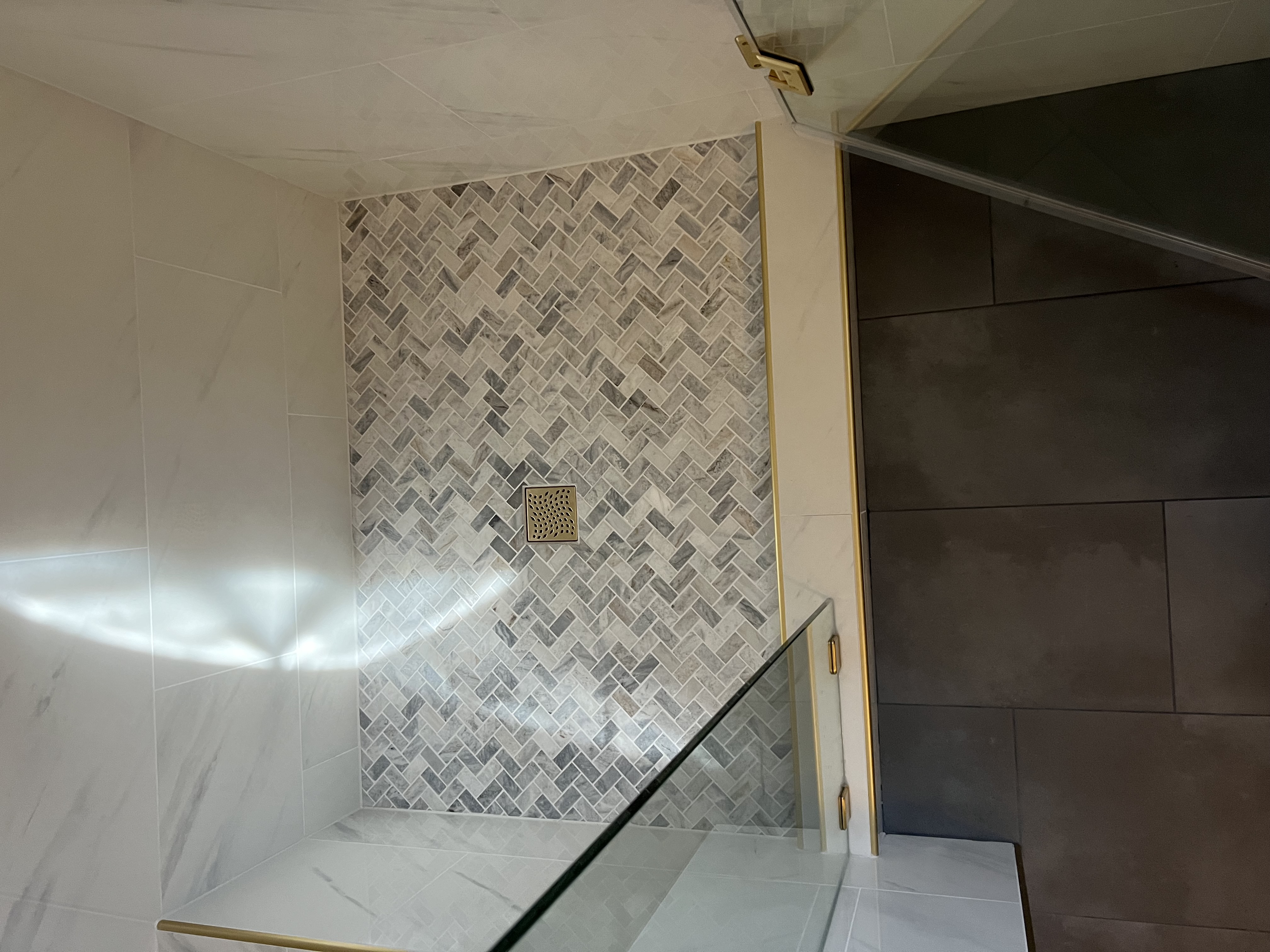 Herringbone mosaic shower floor with gold drain by Level Up Tile