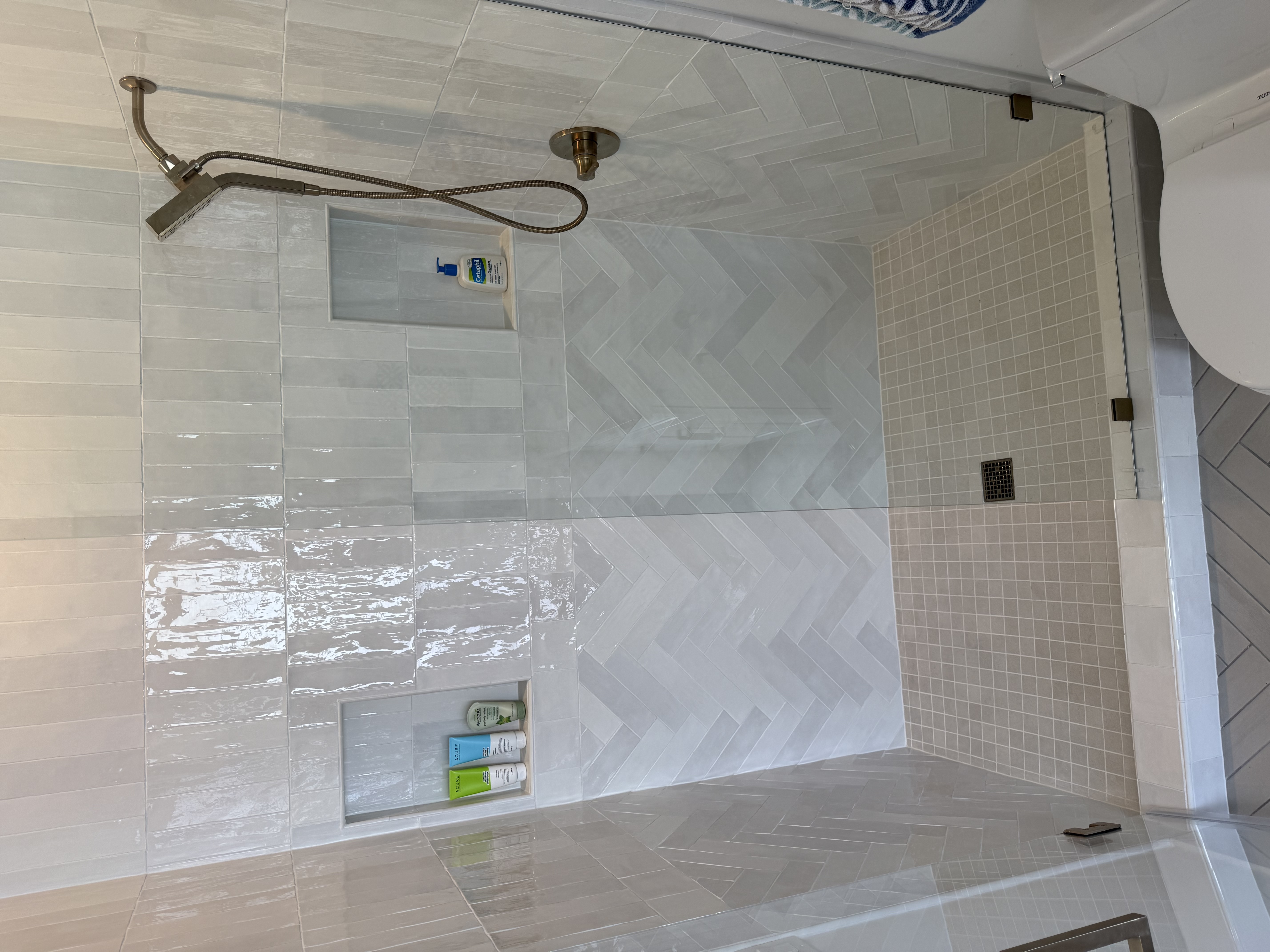 White herringbone shower with gold fixtures by Level Up Tile in Peoria AZ
