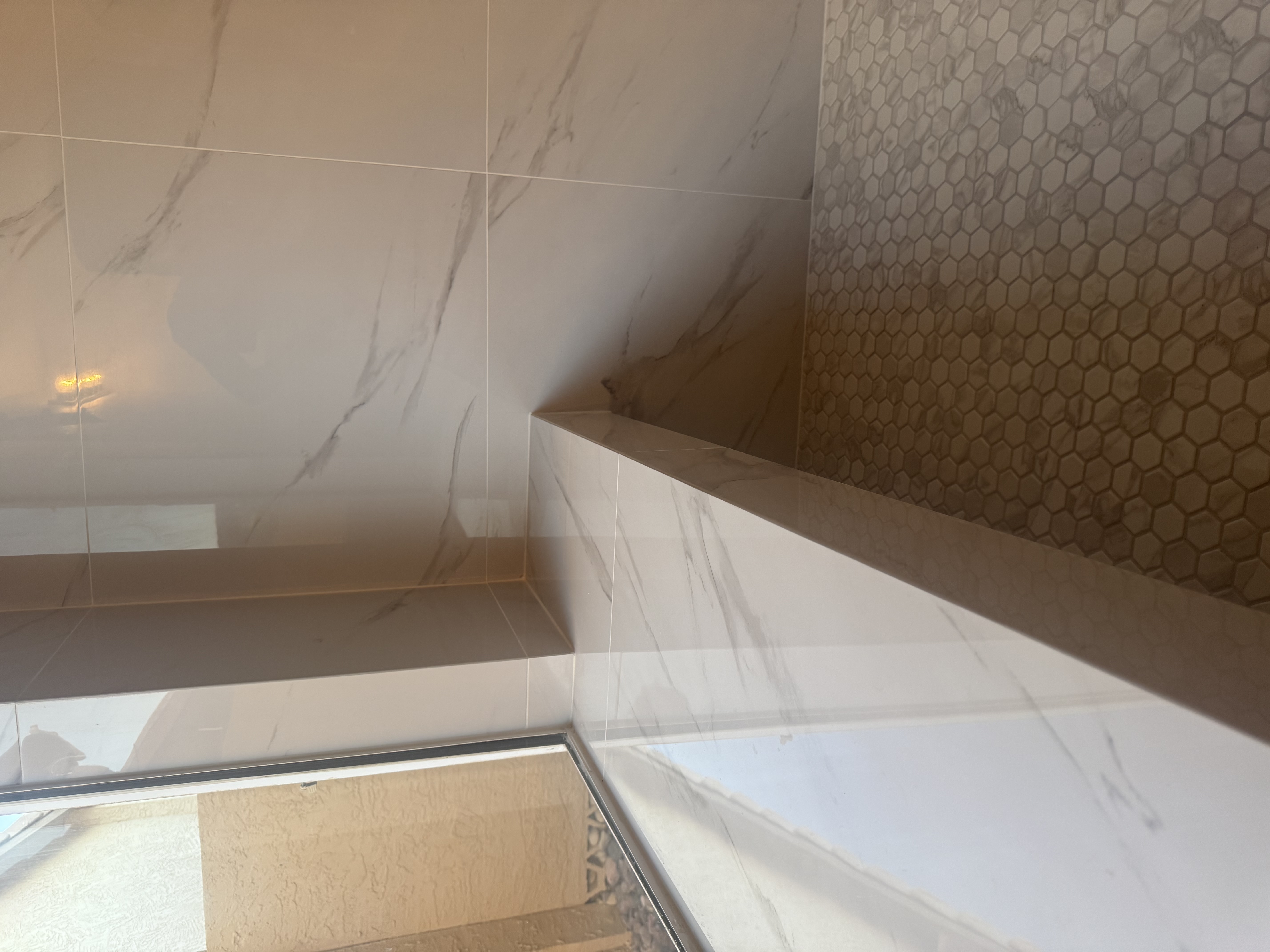 White marble shower bench with hexagonal accent tile by Level Up Tile