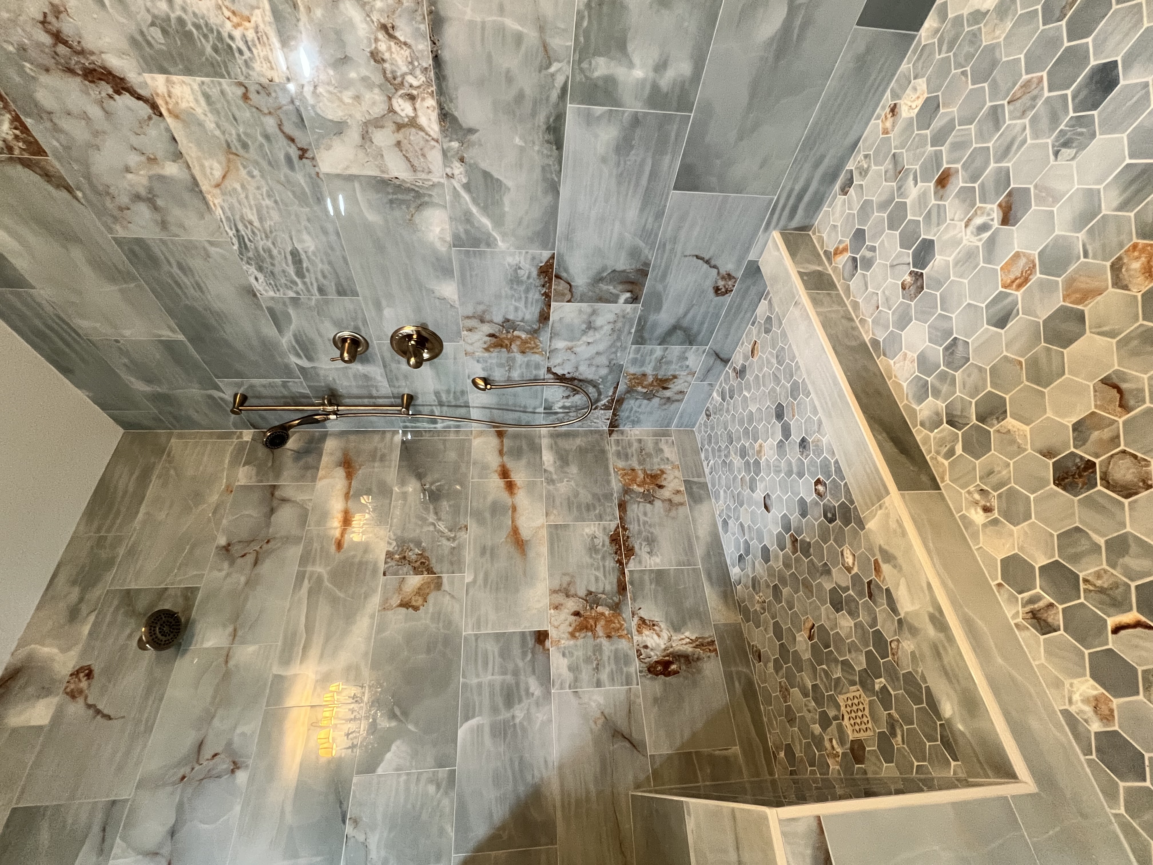 Onyx marble shower with hexagonal accent wall and bench by Level Up Tile