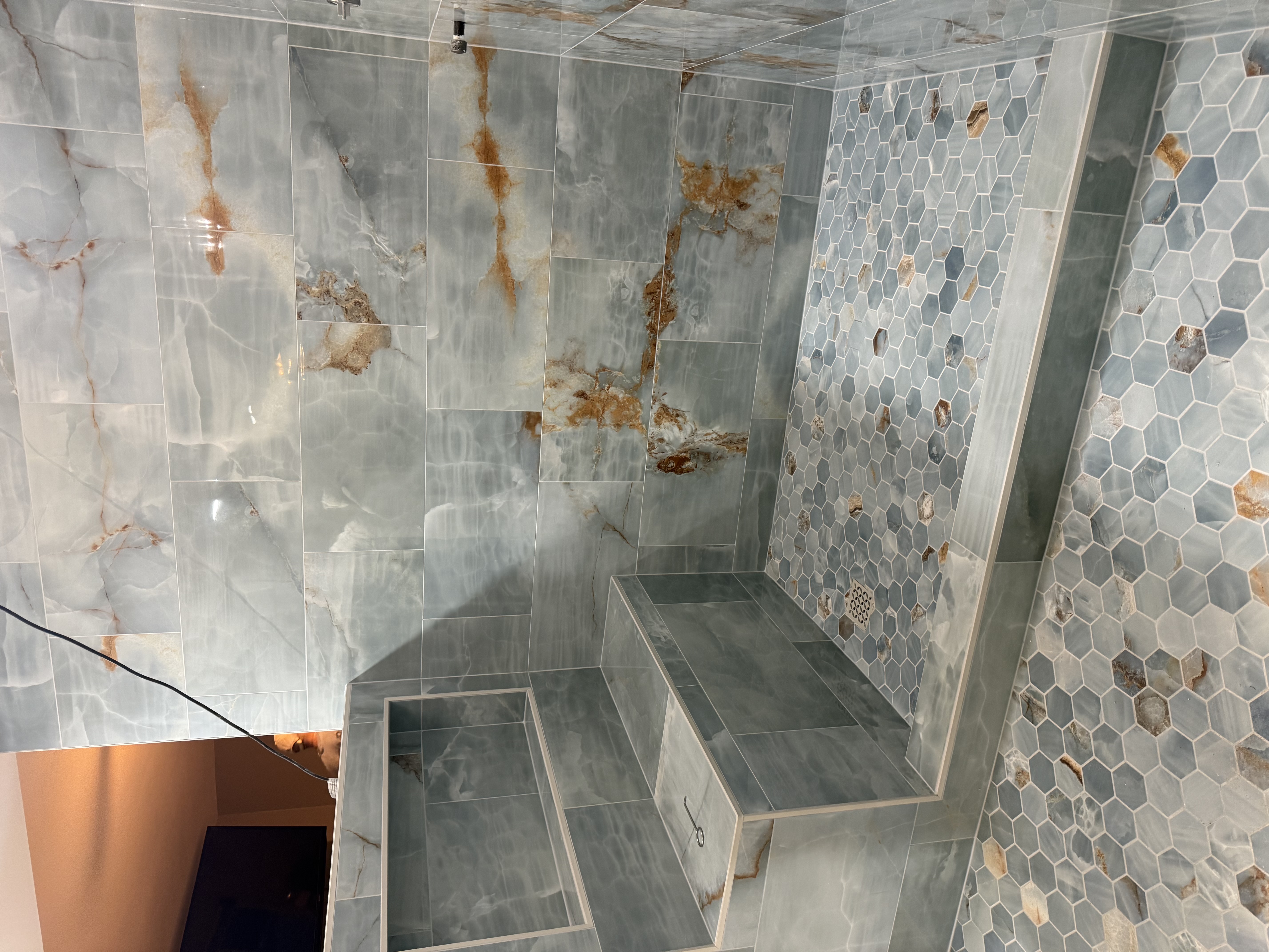 Wide angle view of onyx marble shower with hexagonal accent wall by Level Up Tile